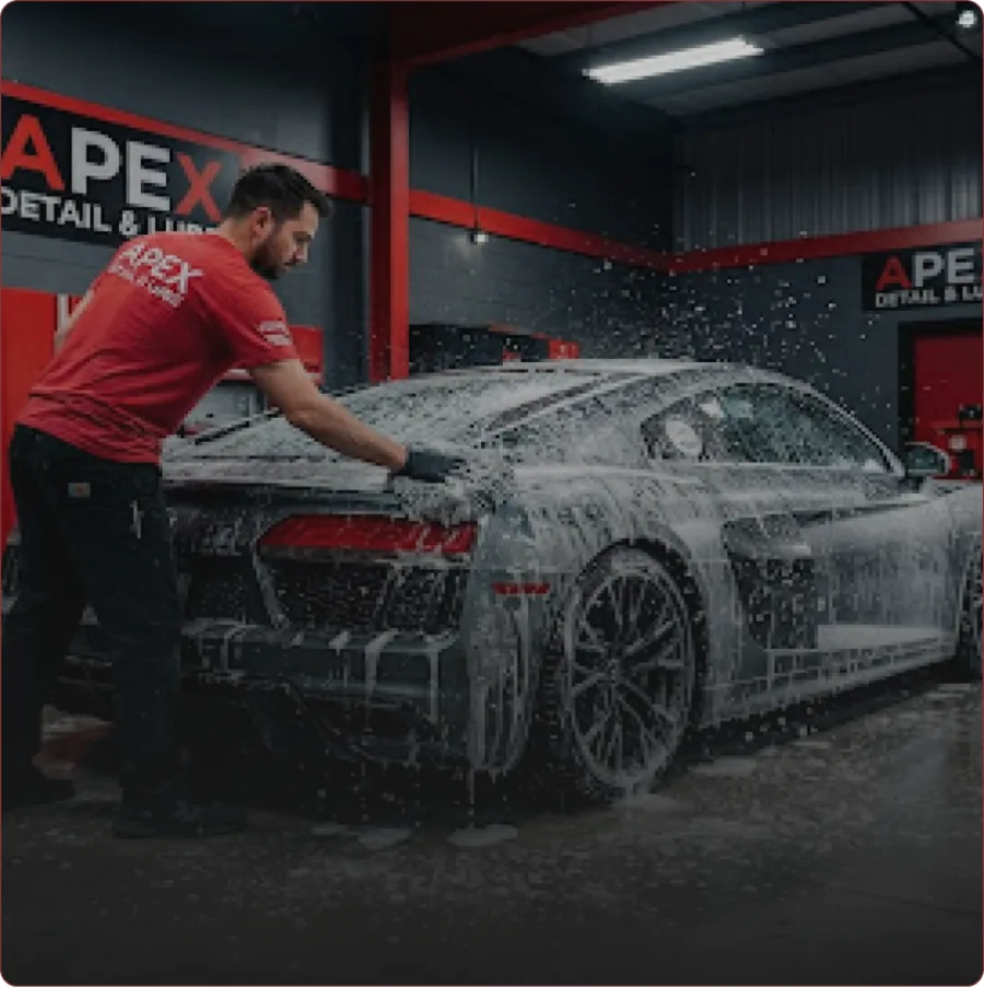 A detailer covering a sports car in cleaning foam